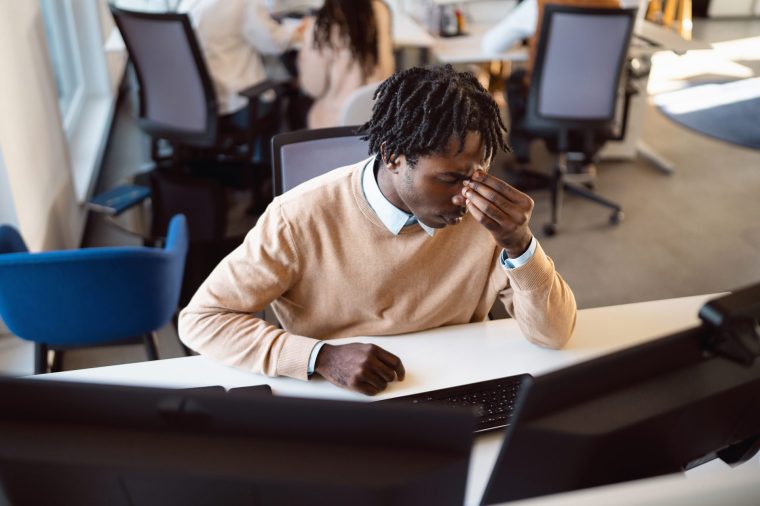 Stressed Black Businessman Working on a Computer at the Desk in an Open-Plan Office - stock photo