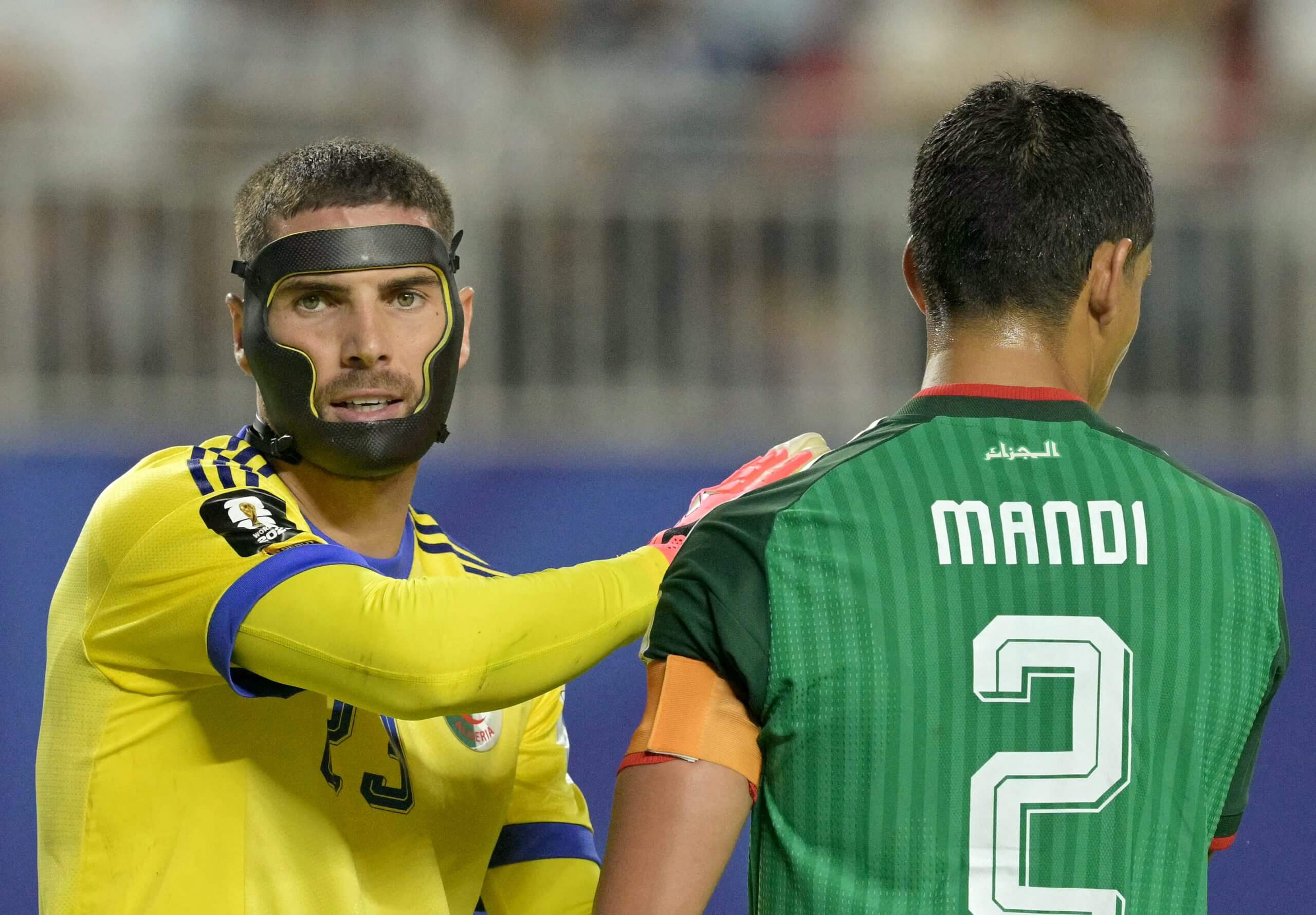 A goalkeeper with a mask on pats his team-mate on the shoulder