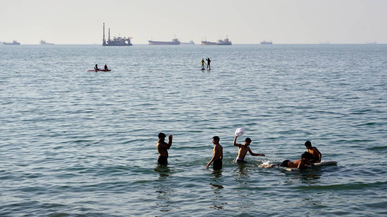 Residents swim and play in the waters of the Strait of Hormuz while cargo ships and commercial vessels lie anchored in the distance off Bandar Abbas, Iran, Wednesday, June 10, 2026.(Razieh Poudat/ISNA via AP)