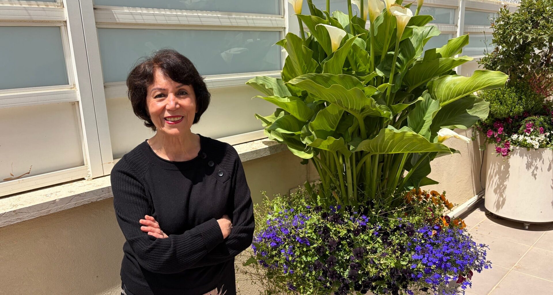 Artist Farideh Golbahar with the flowers she tends at her Jerusalem home, May 2026 (Jessica Steinberg/Times of Israel)
