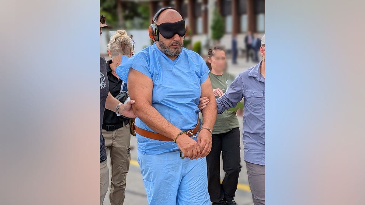 Ibrahim Khaldoon Hilmi being escorted while blindfolded and in handcuffs