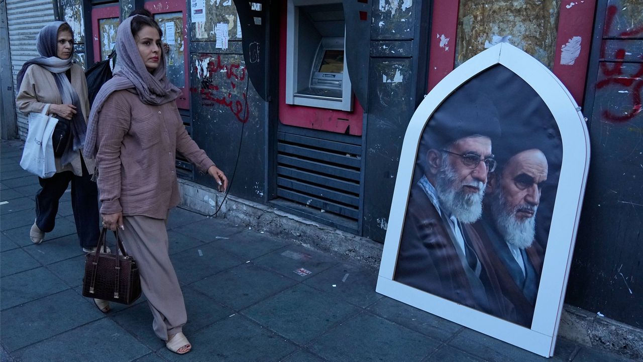 Pedestrians walk past a poster showing the slain Iranian Supreme Leader Ayatollah Ali Khamenei, left, and the late revolutionary founder Ayatollah Khomeini on a sidewalk at the Islamic Revolution square in Tehran, Iran, Sunday, June 14, 2026. (AP Photo/Vahid Salemi)