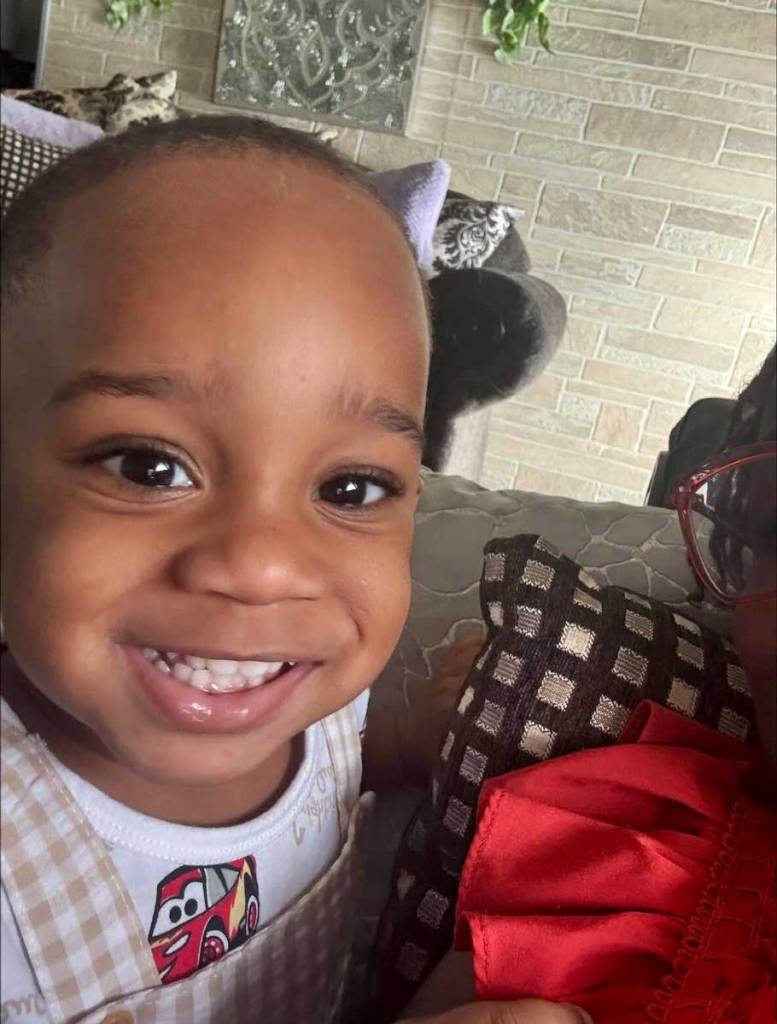 Kohen Wiley in a cars themed outfit smiles on the couch next to a family member
