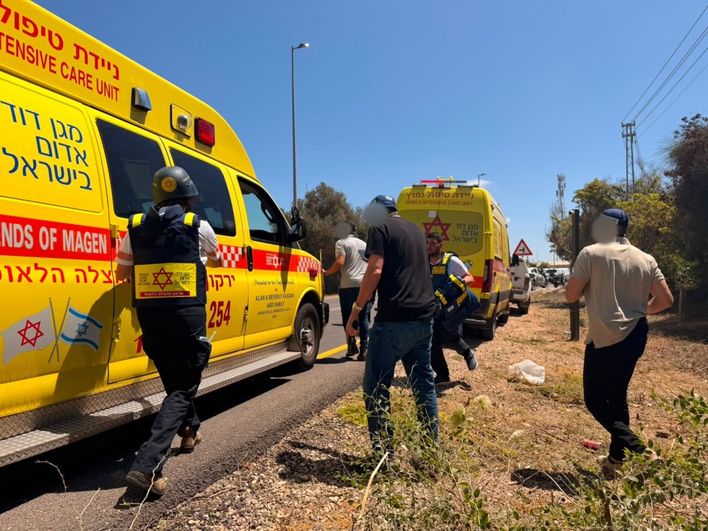 Two Magen David Adom ambulances and several people, some in uniform, next to a road.