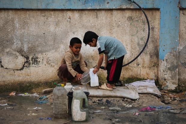 Palestinian children fill plastic bottles with water at a tent camp.