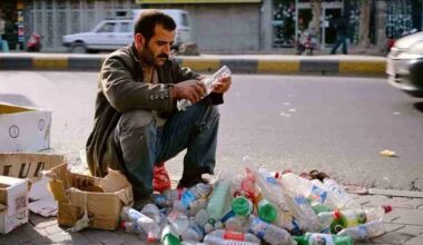 Man crouching on a city street in Iran, sorting through a pile of discarded plastic bottles to scrape together a basic livelihood