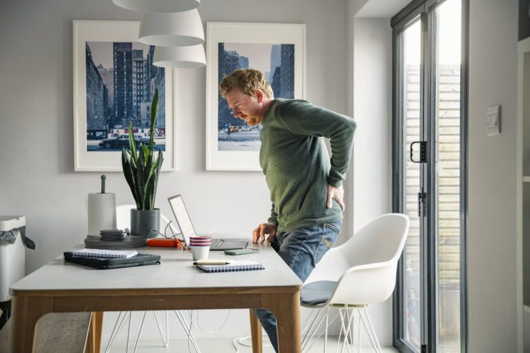A man stands up whilst working from home, holding his back