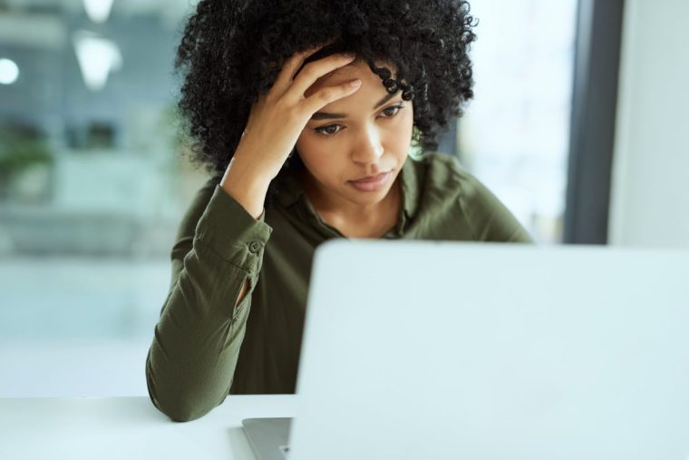 Shot of a young businesswoman looking stressed while using a laptop in a modern office