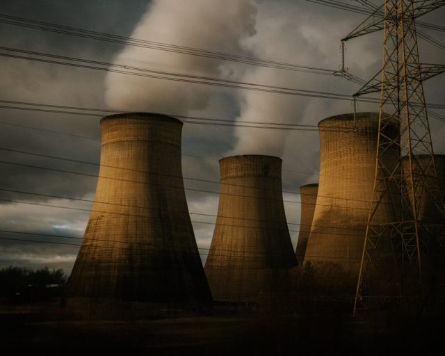 A conceptual, simple image of several huge chimneys in a power plant, releasing waste into the atmosphere. Beside them stands huge electric power masts.