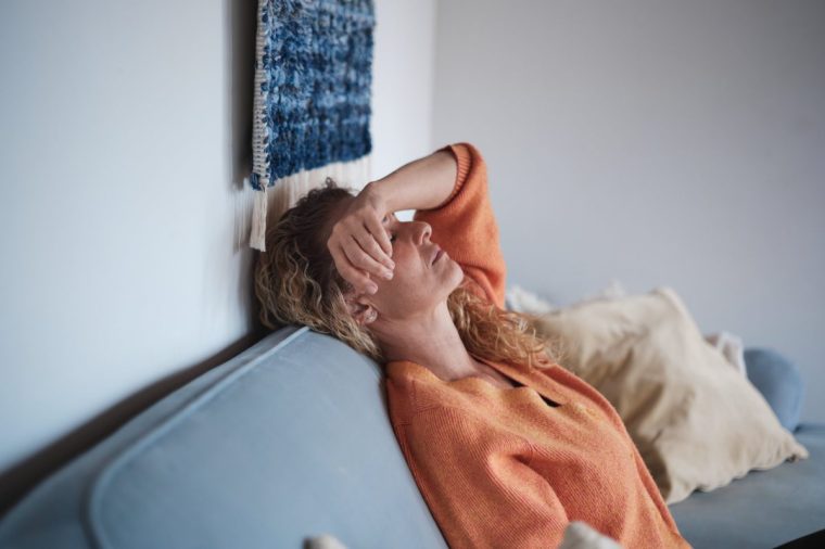 A woman lies back on a couch with her arm over her eyes