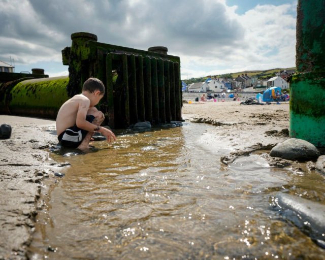 BORTH, WALES - AUGUST 10: Summer holidaymakers play and relax on Borth Beach next to a storm overflow pipe that discharges into the sea on August 10, 2023 in Borth, Wales. There were more than 80,000 sewage overflows into Welsh seas and rivers for more than 500,000 hours in 2022 Surfers reported gastric illnesses after using beaches including Borth Beach. Dwr Cymru, which is responsible for managing water across most of Wales, blames aging infrastructure and the Welsh climate of high rainfall for overflows and has recently installed 2,300 monitors to help reduce the problem. (Photo by Christopher Furlong/Getty Images)
