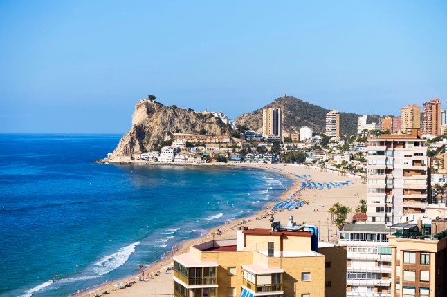 Benidorm cityscape with many tall buildings along the sandy beach, featuring people enjoying the sunny Mediterranean Sea