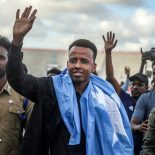 Somali international referee Omar Abdulkadir Artan waves to supporters while draped in the Somali flag as he is welcomed ahead of a solidarity football match after returning to Somalia in Mogadishu on June 10, 2026. Somali referee Omar Artan, who was denied entry to the United States for the World Cup, returned to a hero's welcome in Mogadishu and vowed to take part in the next tournament in 2030. Artan's rejection has sparked outrage at home.Artan, who in 2025 was named men's referee of the year by the Confederation of African Football (CAF), was barred from entering the US on Saturday after arriving at Miami International Airport. (Photo by Hassan Ali Elmi / AFP via Getty Images)