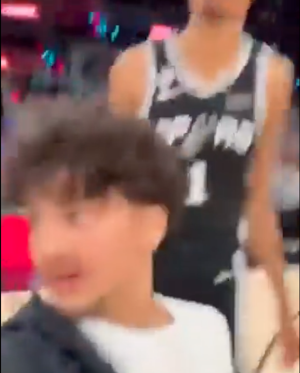 A young boy with curly hair in a white shirt and a blurred person in a number 1 sports jersey.