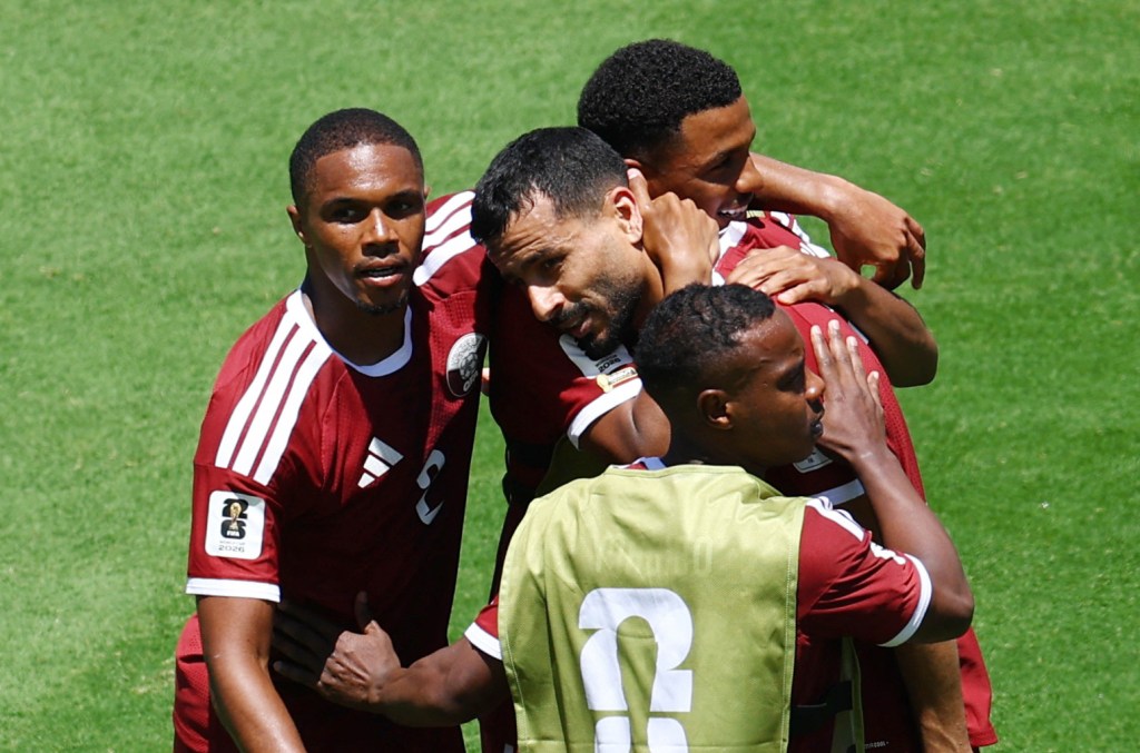 Four soccer players from Qatar celebrate a goal during a FIFA World Cup 2026 match against Switzerland.