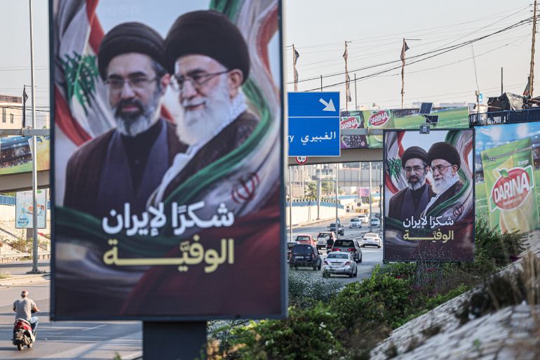 Cars and motorbikes drive past billboards showing Iran’s new Supreme Leader Ayatollah Mojtaba Khamenei (L) and his late father Ali Khamenei (R), with the slogan “Thank you, loyal Iran,” erected along the highway leading to Rafic Hariri International Airport in Beirut on June 22, 2026.