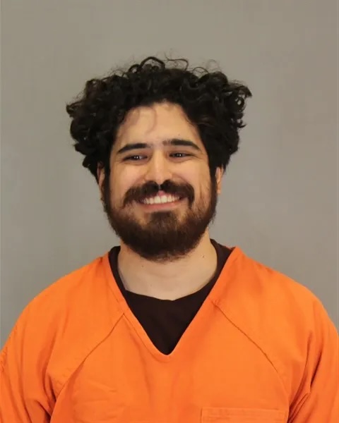 Mugshot of Abraham Alvarez, a smiling man with dark curly hair and a beard, wearing an orange jumpsuit.
