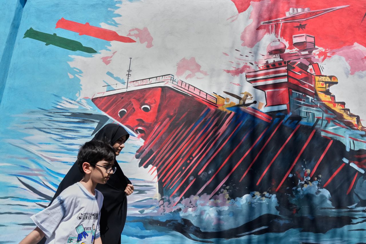 People walk past a mural depicting a U.S. aircraft carrier under missile attack in downtown Tehran, Iran, on Monday.