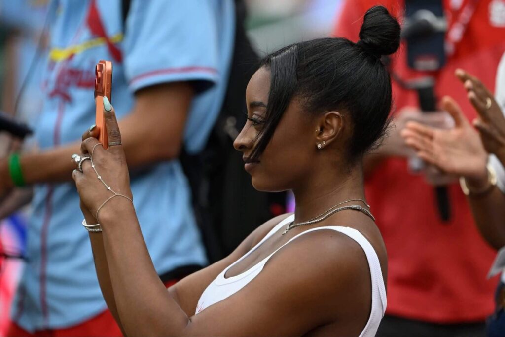 Simone Biles holds up a cellphone to take a photo before a game between the St. Louis Cardinals and the Chicago Cubs.