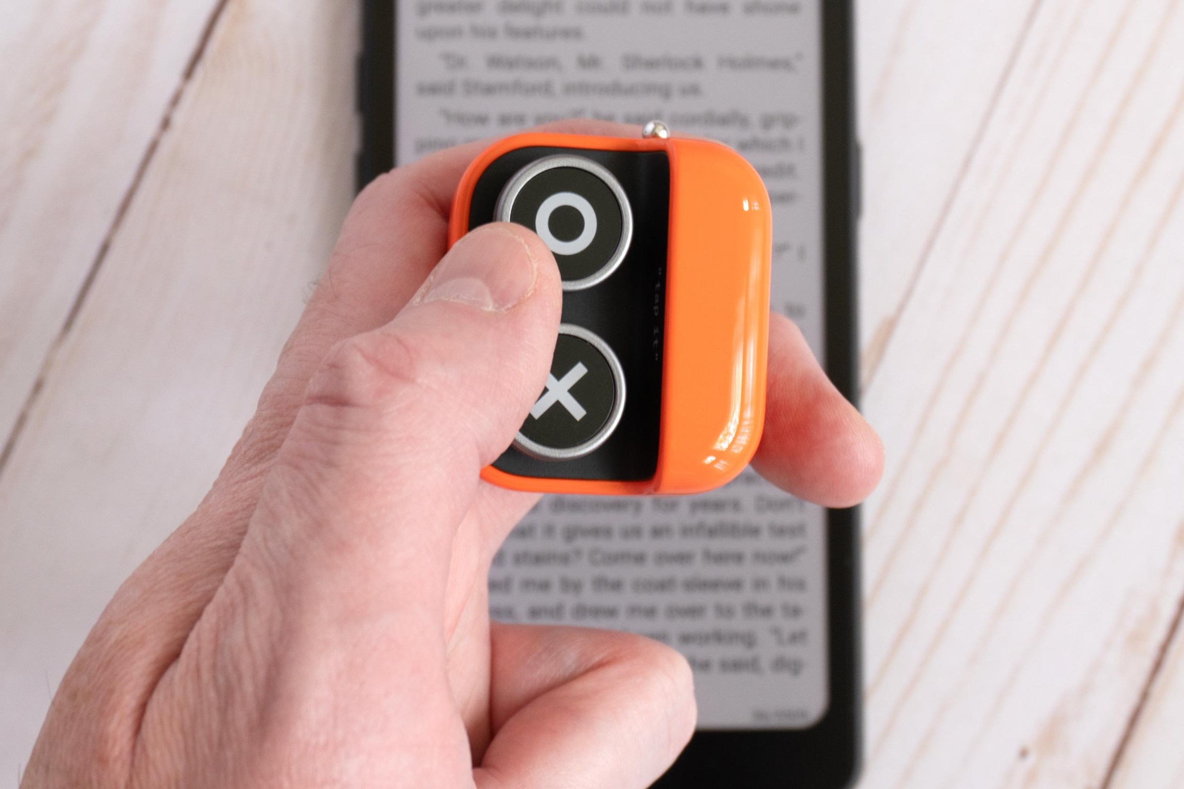 A person holding and pressing a button on the Boox Tappy with an e-reader in the background.