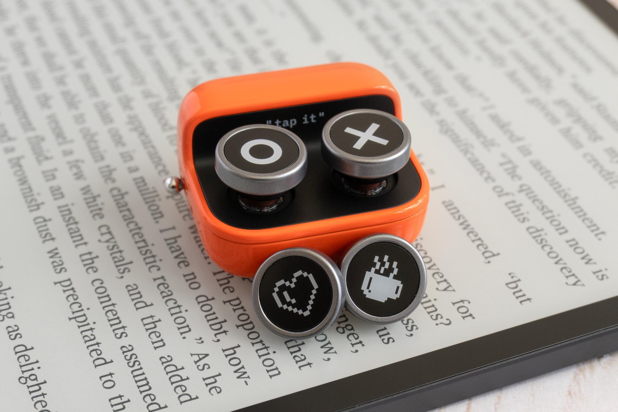 The Boox Tappy on an e-reader next to the included alternate button designs.