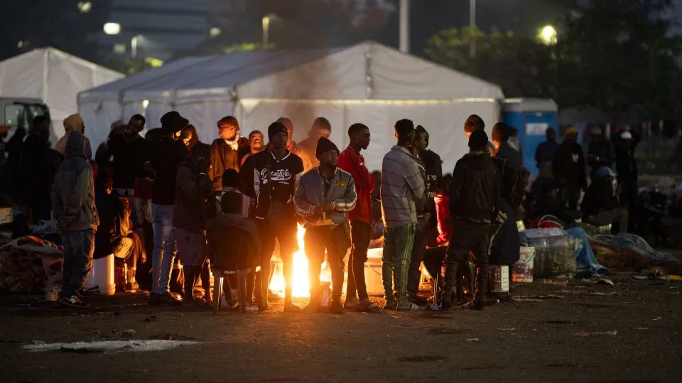 Undocumented migrants warm up by a camp fire in Durban on June 27, as they wait to be registered by South African immigration officers ahead of their repatriation. - Marco Longari/AFP/Getty Images