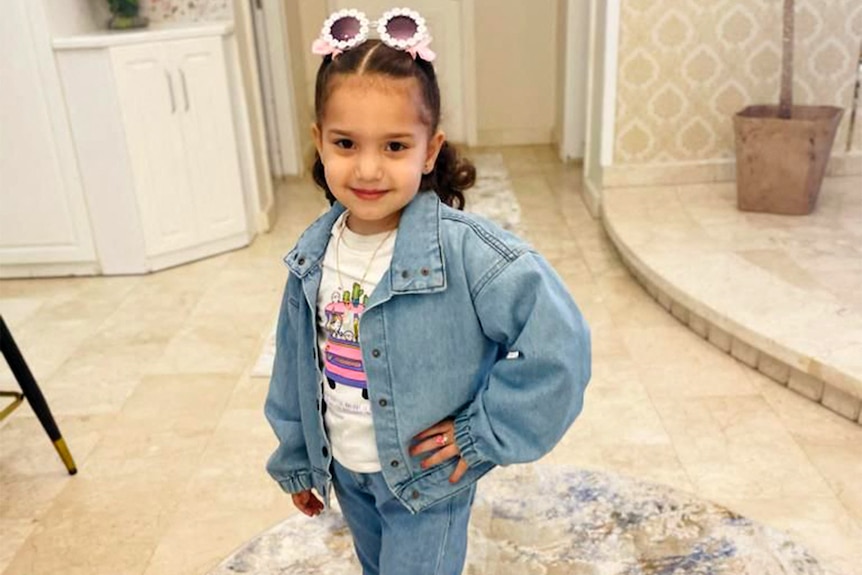 A young girl posing in a denim jacket and novelty sunglasses.