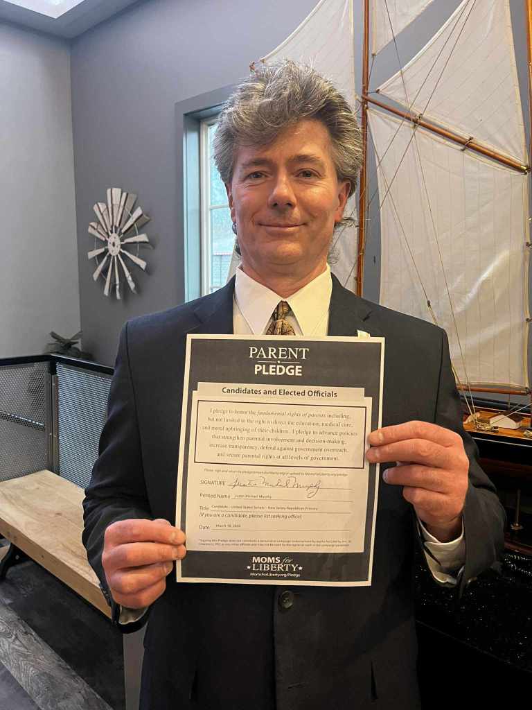 Justin Murphy holding a Moms for Liberty "Parent Pledge" for candidates and elected officials.