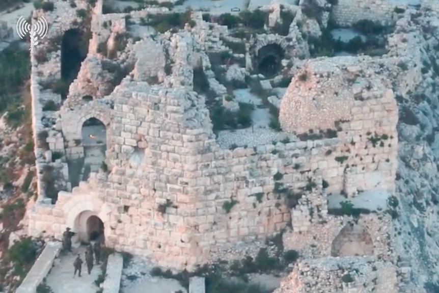 Israeli soldiers walking along a concrete bridge into a medieval castle atop a mountain ridge.