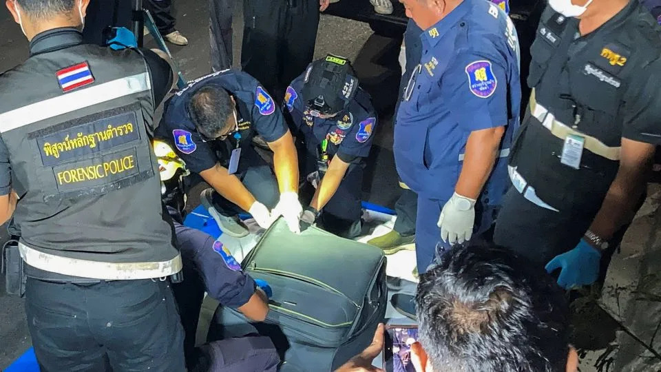 Forensic technicians examine a suitcase, in which police later found the body of a 17-year-old Thai girl, after it was recovered from a grassy area near a railway track in Pattaya City, on June 27. - Teerasak Suttativong/Reuters