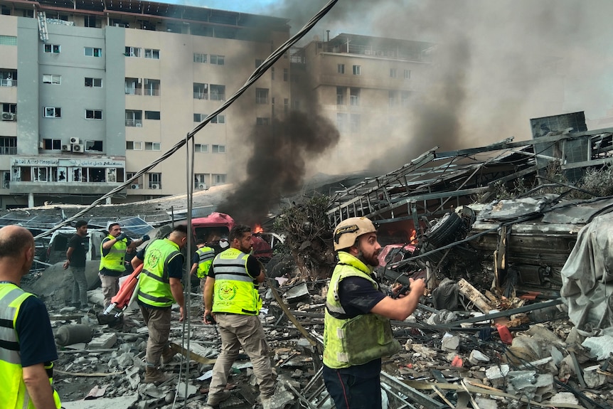 People wearing hi vis clothes walk through smouldering rubble.