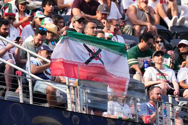 Iran An attendees holds an Iranian flag with an "X" on it before the World Cup Group G soccer match between Iran and New Zealand in Inglewood, Calif., near Los Angeles, Monday, June 15, 2026.