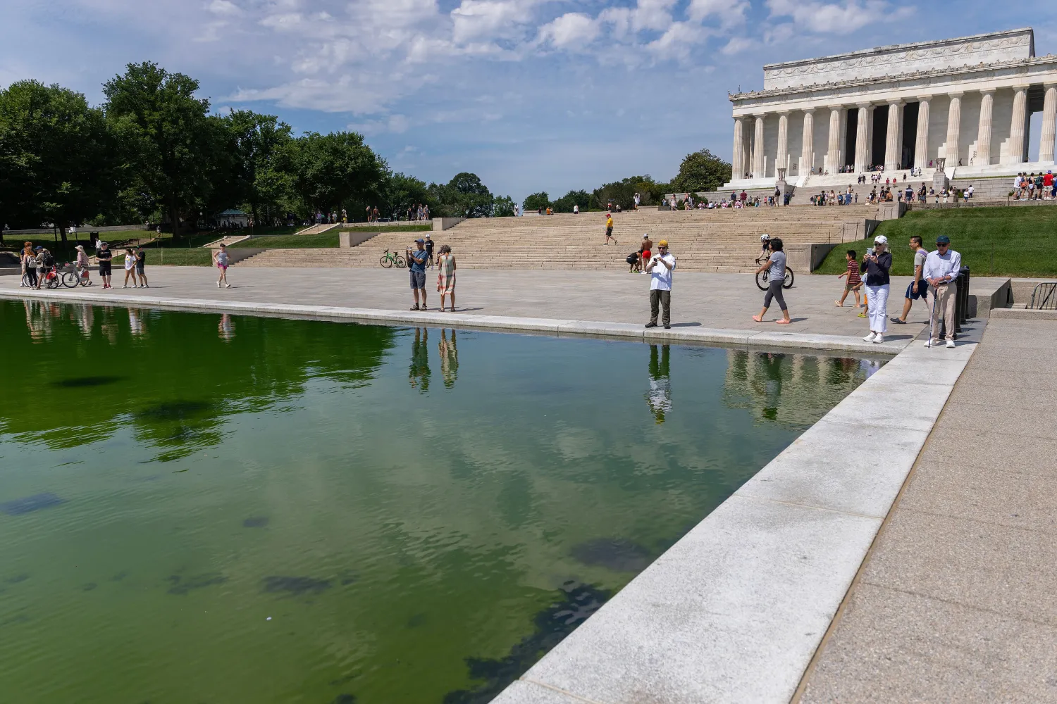 People walk along the Lincoln Memorial Reflecting Pool where algae has begun to bloom following the completion of recent renovations on June 14, 2026 in Washington, DC.