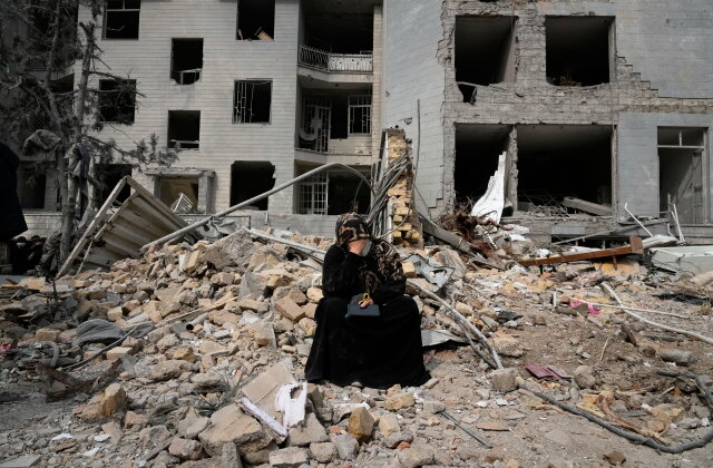 A woman sits on rubble across from a residential building damaged last Sunday during the U.S.-Israeli air campaign in Tehran, Iran, Thursday, March 12, 2026. (AP Photo/Vahid Salemi)