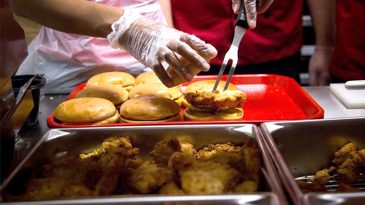 A Chick-fil-A sandwich is poked with tongs on a red tray.