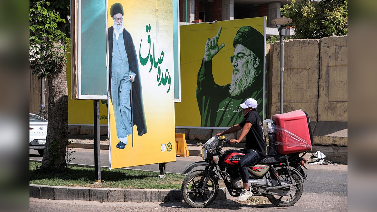 A deliverman drives a motorcycle along a road in Baghdad past billboards of Ali Khamenei and Hassan Nasrallah