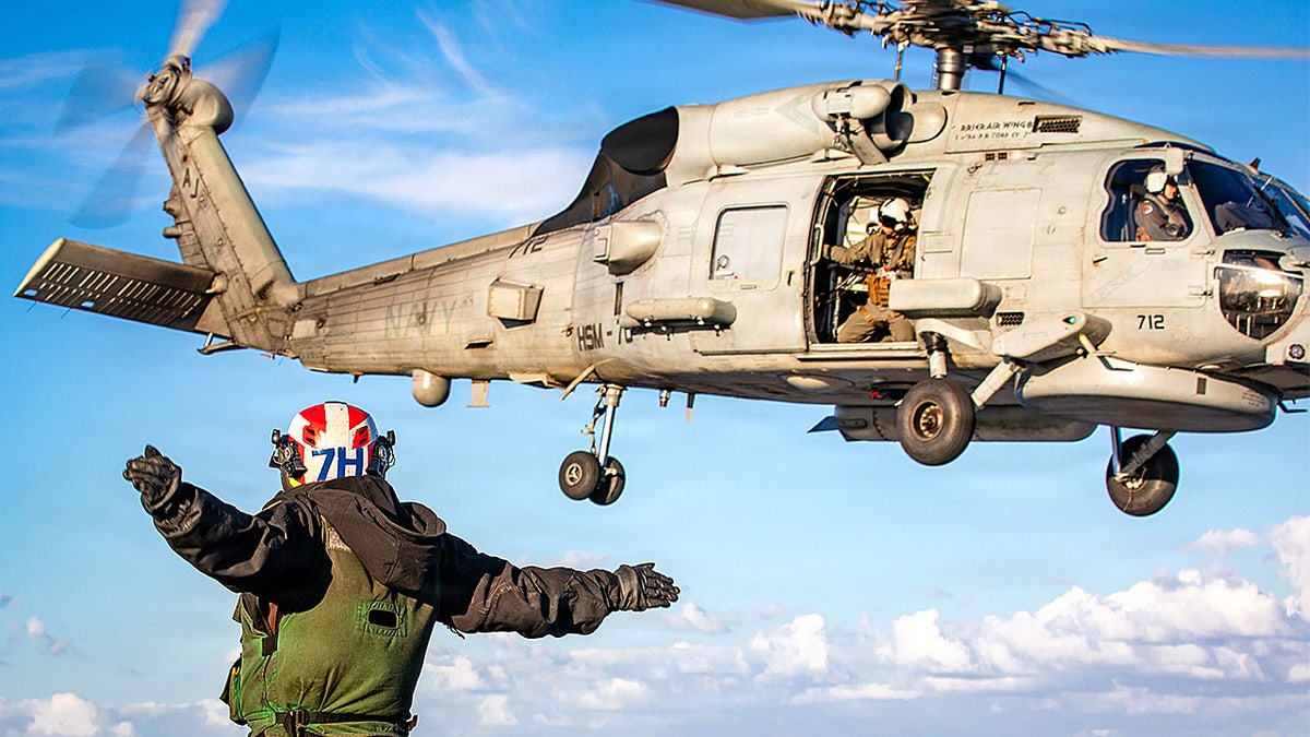U.S. sailor signaling launch of MH-60R Sea Hawk helicopter aboard USS Gerald R. Ford