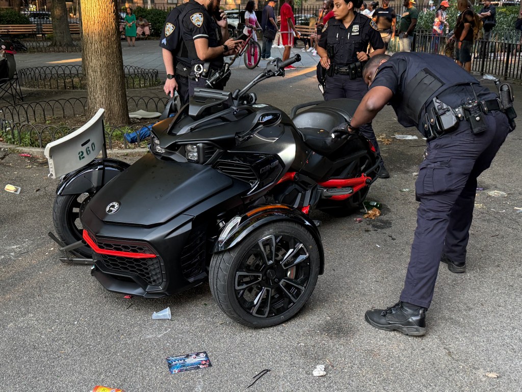 A three-wheeled Can-Am motorcycle in a park, with police officers nearby and litter on the ground.