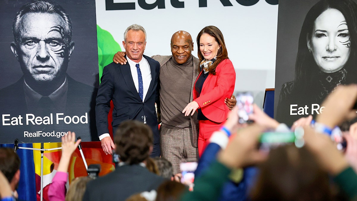 U.S. Secretary of Health and Human Services Robert F. Kennedy Jr. and former boxing heavyweight champion Mike Tyson take photos with Agriculture Secretary Brooke Rollins at an event.