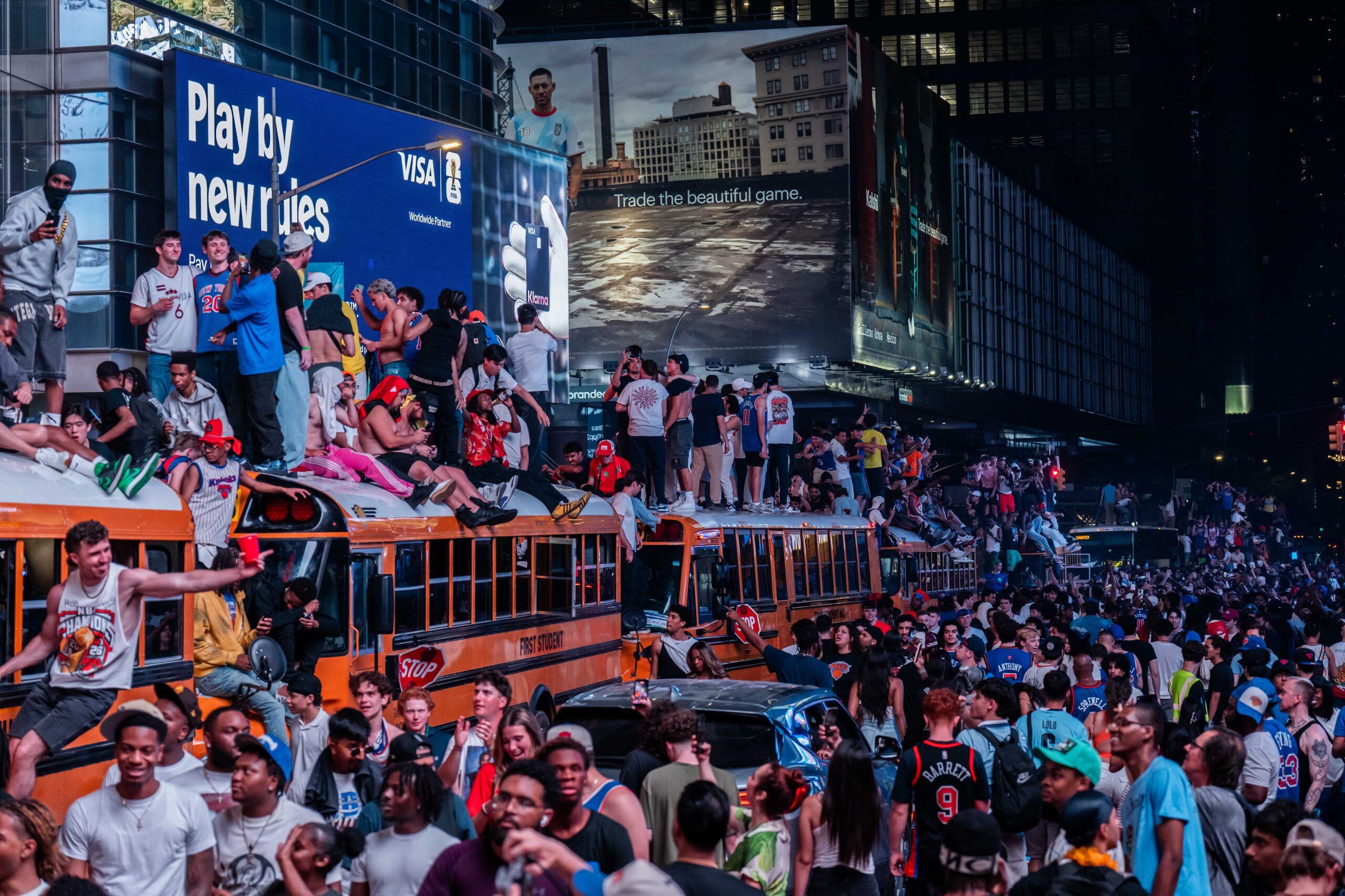 Hundreds of fans sitting on top of or standing around yellow school buses in New York City