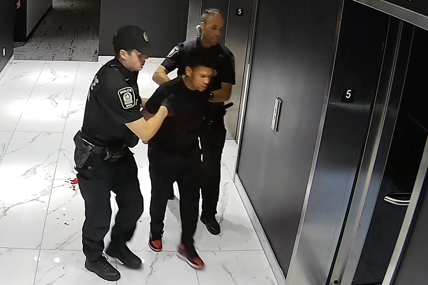 Two police officers walk a man in handcuffs to an elevator.