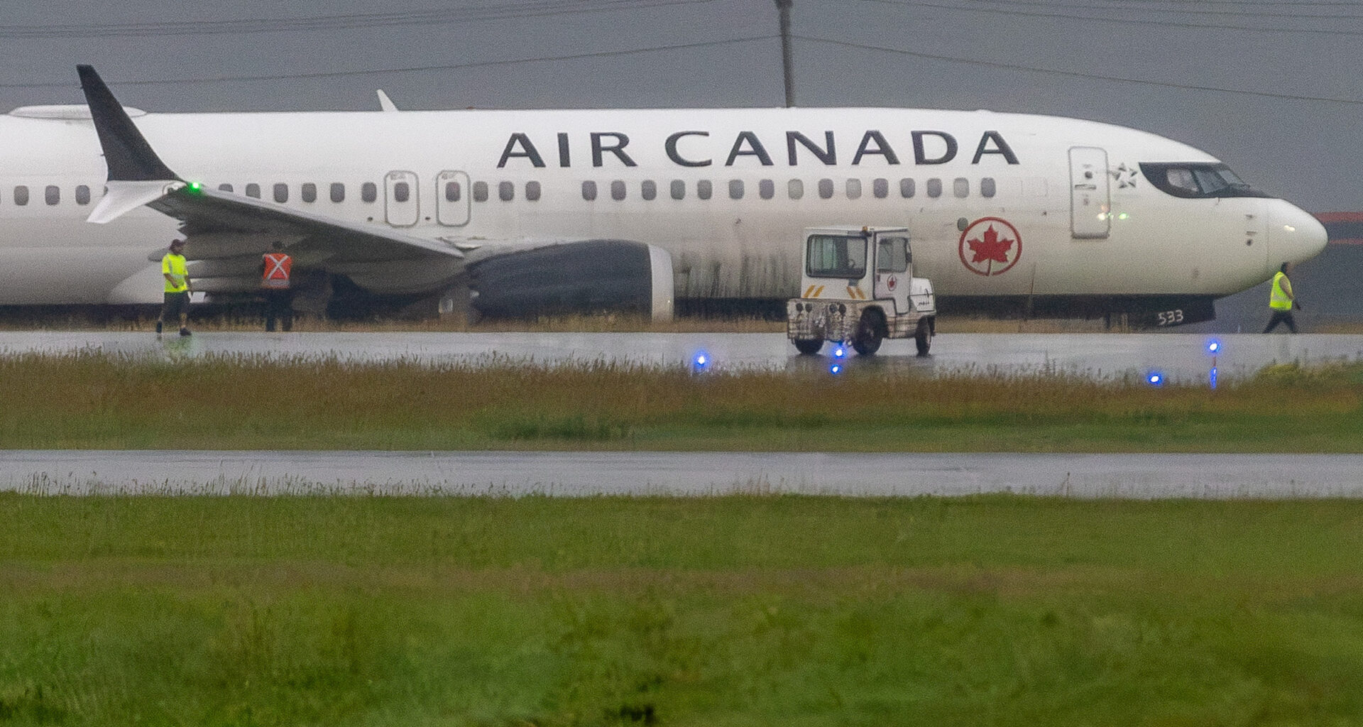 An Air Canada plane in the grass next to a taxiway.