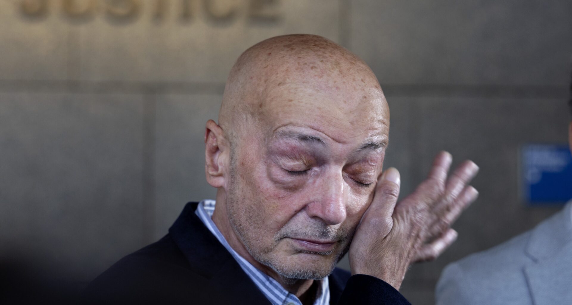 Man wipes away tears from his face with one hand in the corridor of a courthouse.