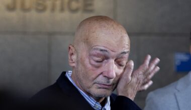 Man wipes away tears from his face with one hand in the corridor of a courthouse.