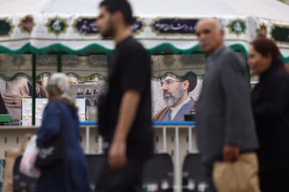 People walk in front of a banner of Supreme Leader Mojtaba Khamenei in Tehran (May 2026) 