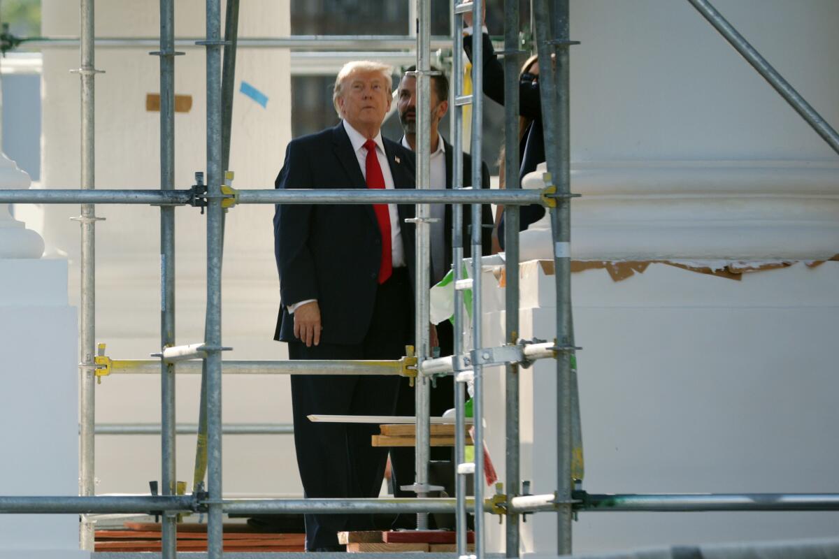 President Trump stands near scaffolding and looks up.