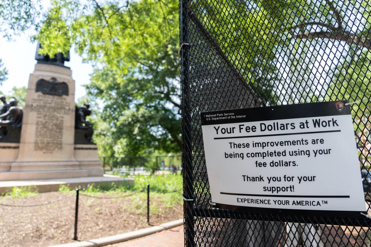 A sign on a fence reads, "These improvements are being completed using your fee dollars."