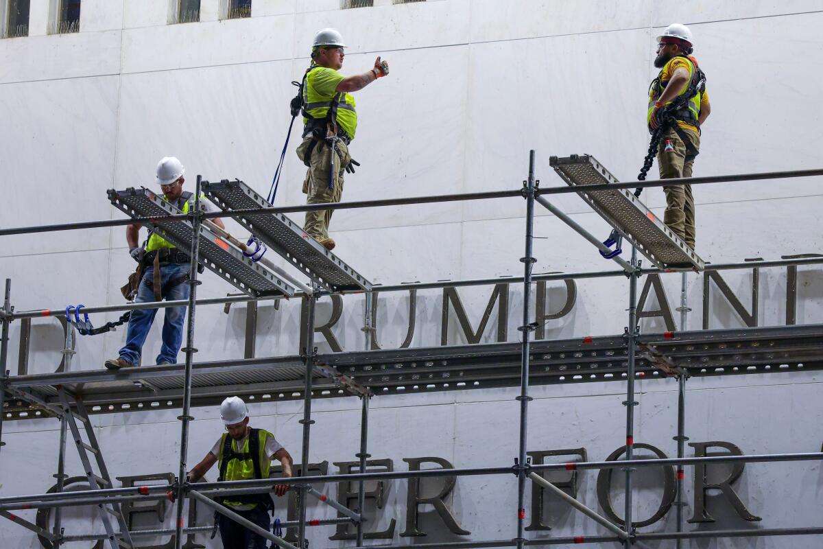 Construction crews stand on scaffolding next to Trump's name on the Kennedy Center.