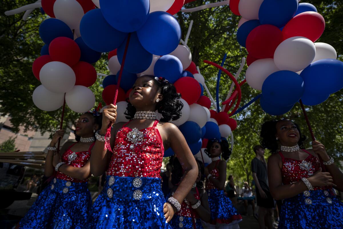 Girls in red and blue sequined dresses hold up red, white and blue balloons.