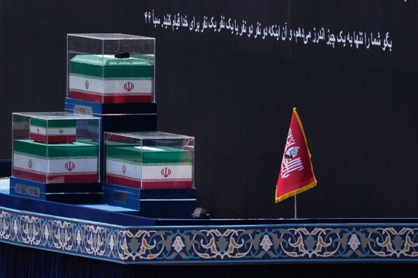 The coffins of the late Iranian Supreme Leader Ayatollah Ali Khamenei and members of his family are displayed on a platform before the start of the dayslong funeral ceremonies at the Imam Khomeini Mosalla Grand Mosque in Tehran, Iran, Saturday, July 4, 2026. A Quran verse in Persian on the backdrop reads, "Say, 'I only advise you of one thing: that you stand for Allah, in pairs or individually.'" (AP Photo/Vahid Salemi)